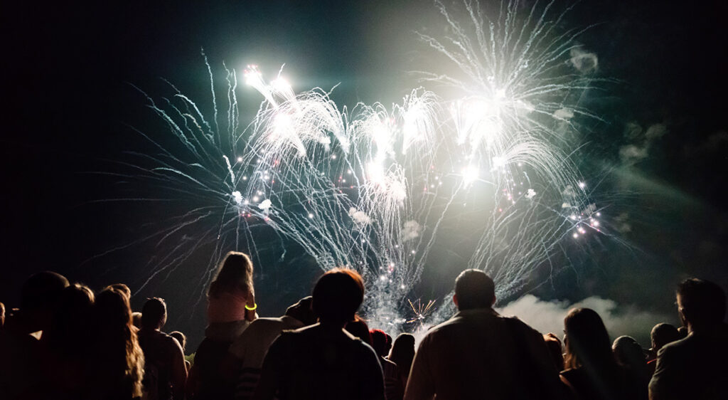group of people gathered watching white, bright fireworks in the night sky