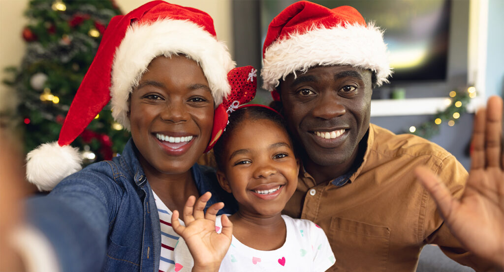 Two adults and one child taking a photo wearing Christmas hats