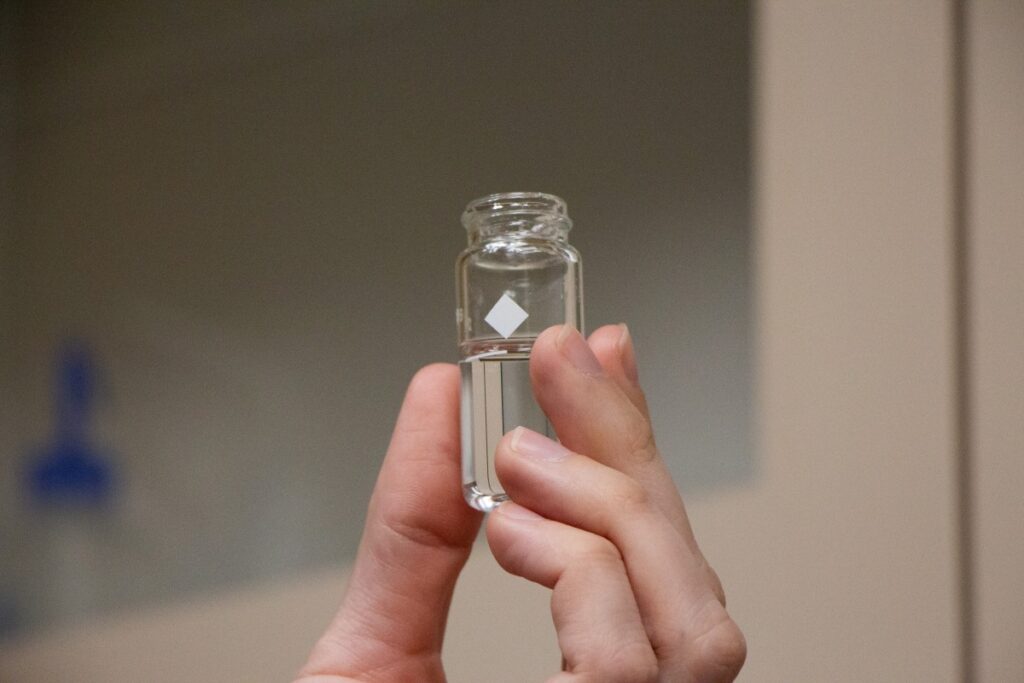 hand holding a small test tube of clear water with white diamond printed on bottle