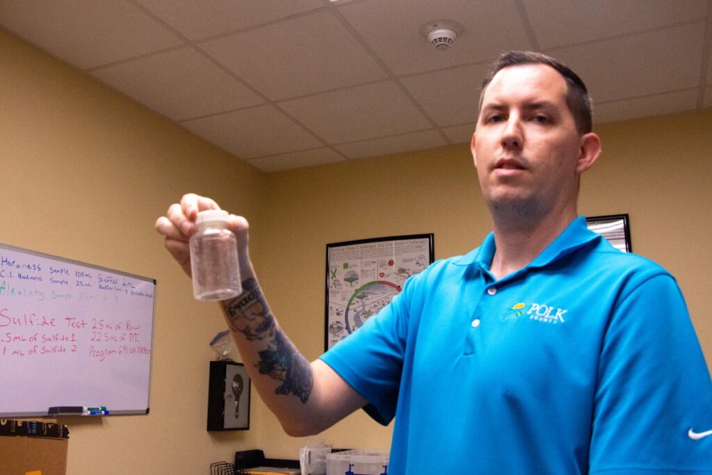Man wearing light blue shirt holding plastic container used for water testing
