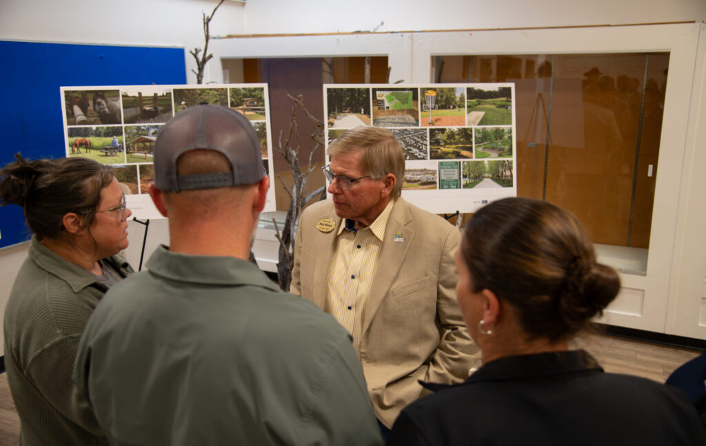 El concejal del condado de Polk, Rick Wilson, conversando con tres personas que se encuentran frente a dos bocetos de diseño durante la reunión pública celebrada el 24 de febrero.