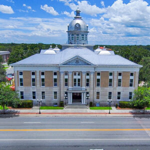 A historic courthouse with a neoclassical façade featuring tall columns, arched windows, and a central dome topped with a clock tower. The light‑colored stone exterior faces a city street lined with lamps and a sidewalk.