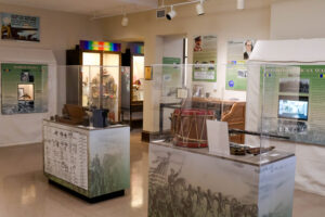 Military history exhibit at the Polk History Center featuring displays on the Spanish-American War and World War I. Artifact cases contain historic uniforms, weapons, a field drum, communication equipment, and military memorabilia, accompanied by interpretive panels highlighting Polk County's military service and veterans.