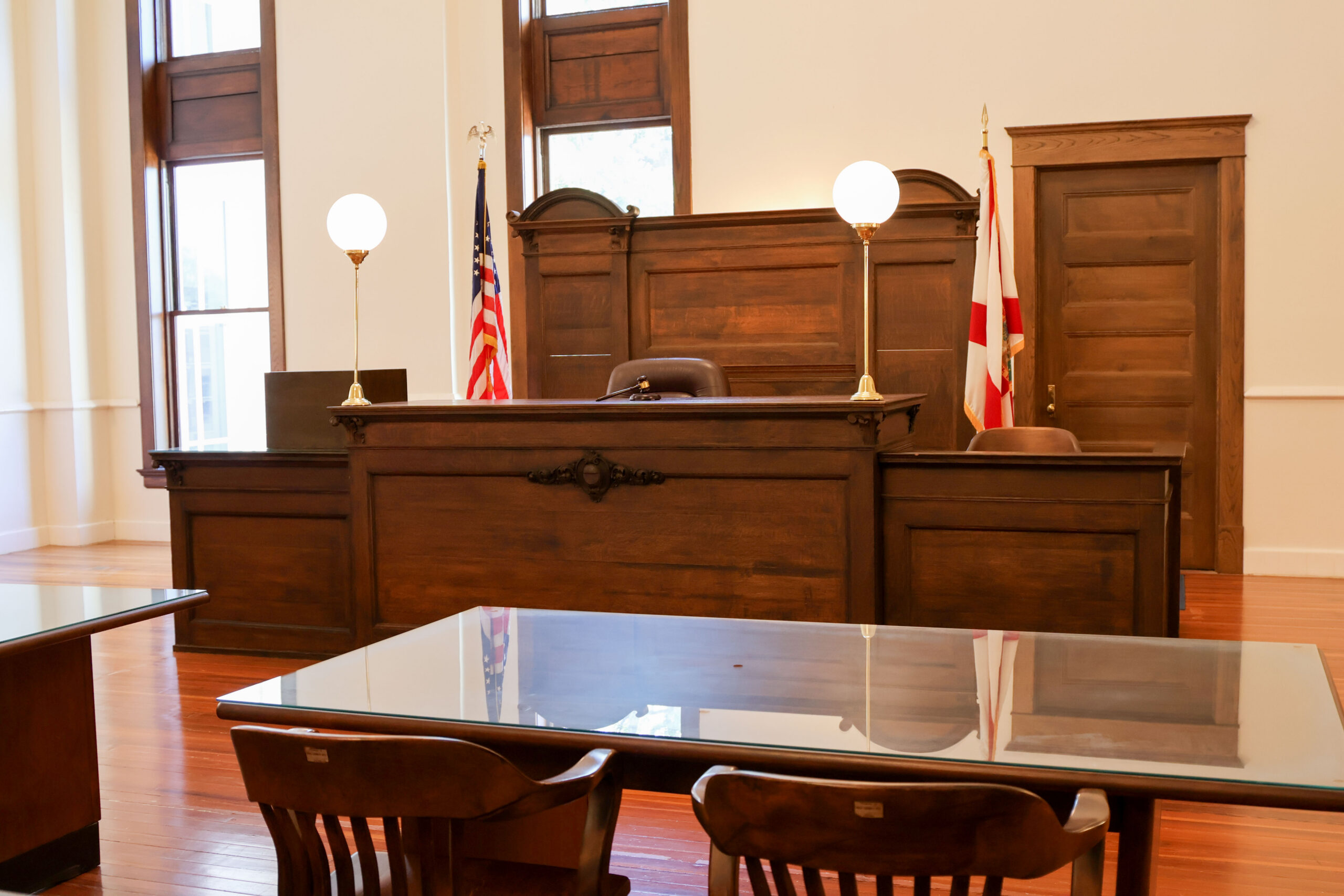 Historic courtroom at the Polk History Center featuring a restored wooden judge's bench, witness stand, jury seating, and polished wood floors. The U.S. and Florida flags stand behind the bench, recreating the appearance of an early 20th-century Polk County courtroom.