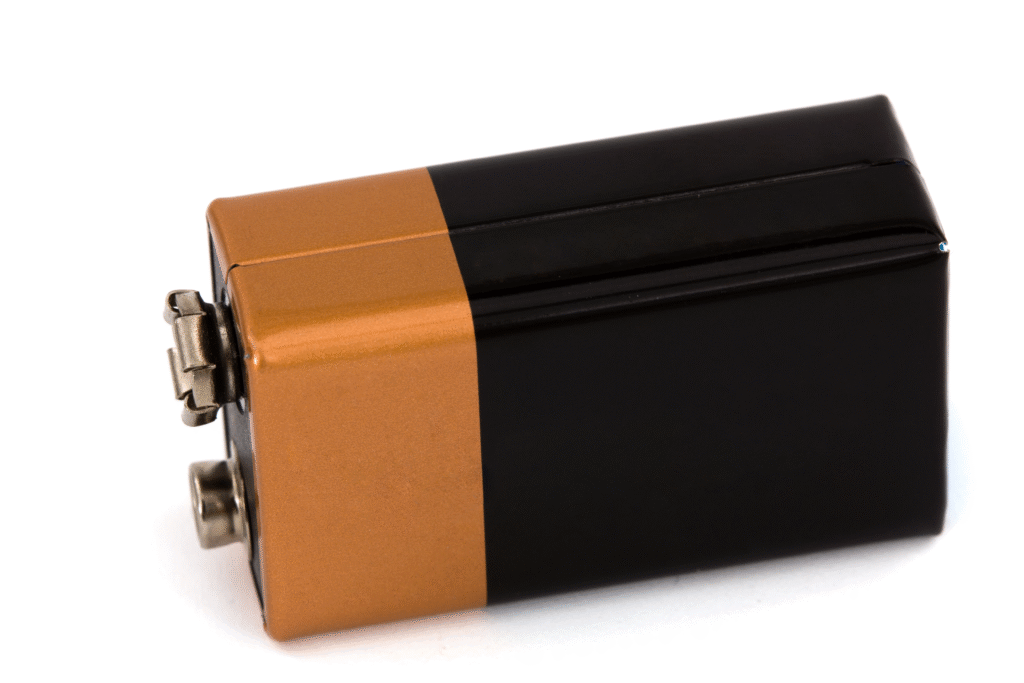 Close-up of a rectangular 9-volt alkaline battery with a copper-colored top, black body and two metal terminals on a white background.